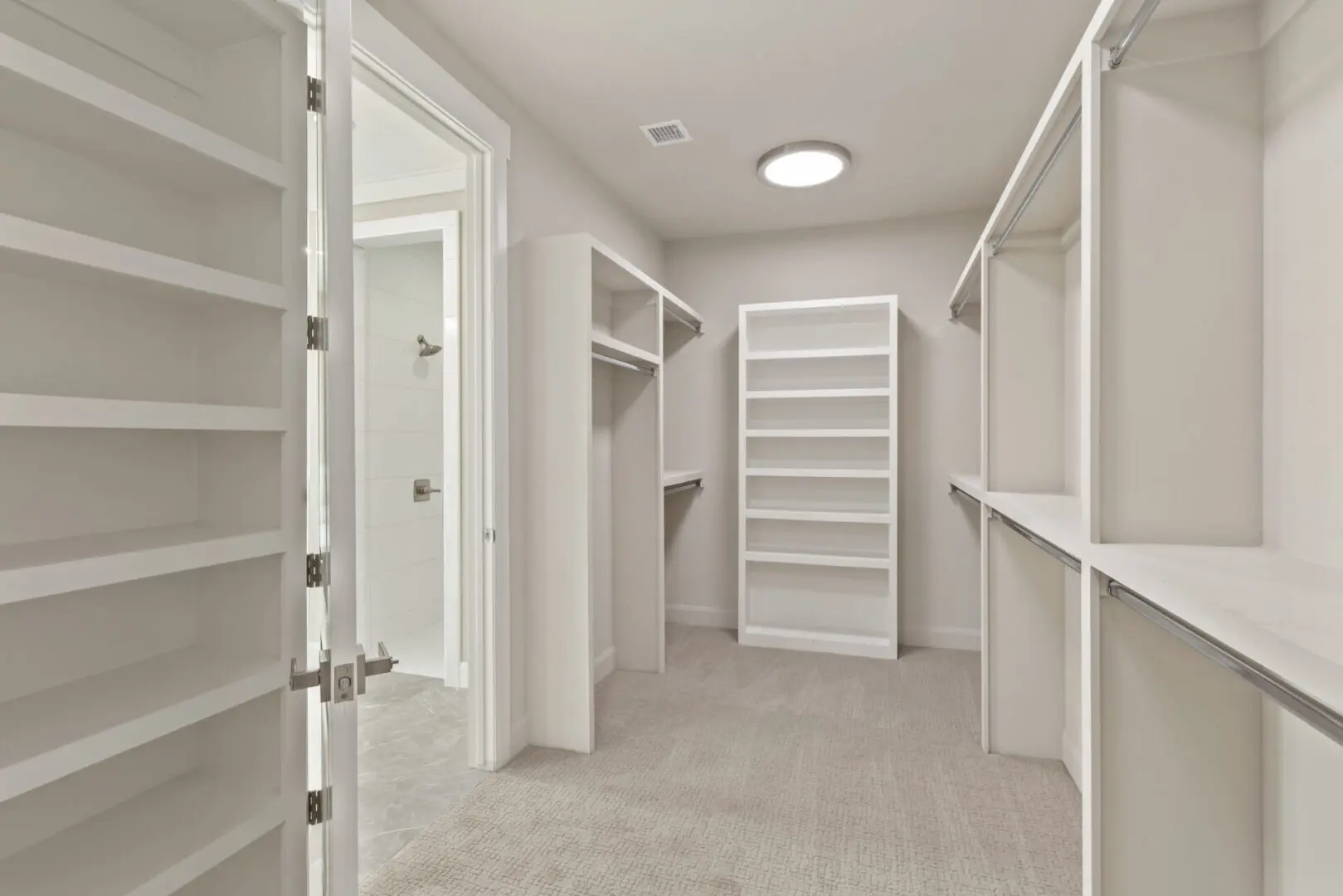 A large walk in closet with white shelving and cabinets.