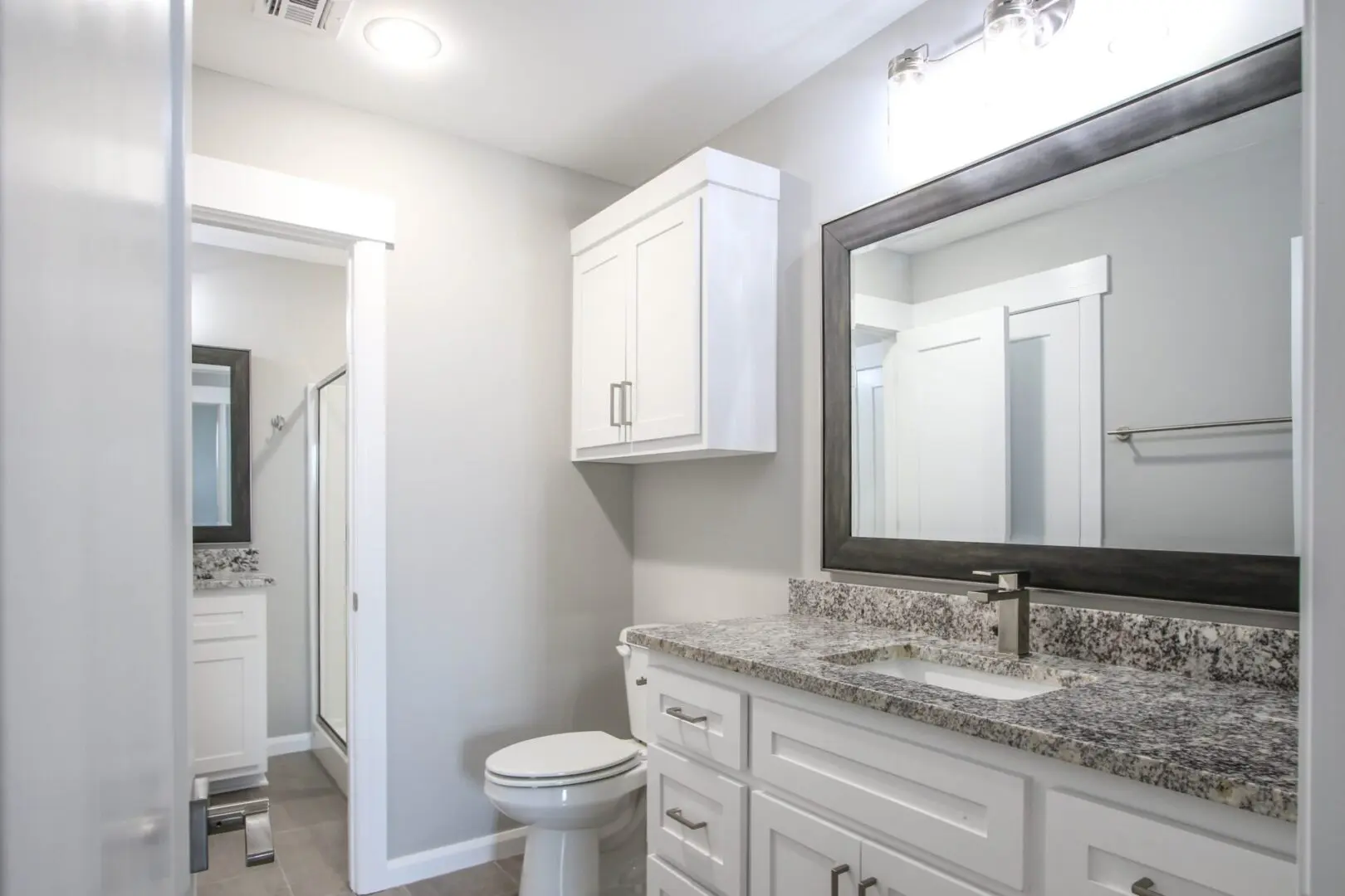 A bathroom with white cabinets and granite counter tops.