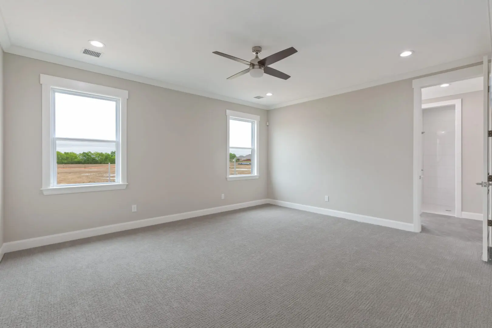 A large empty room with two windows and ceiling fan.